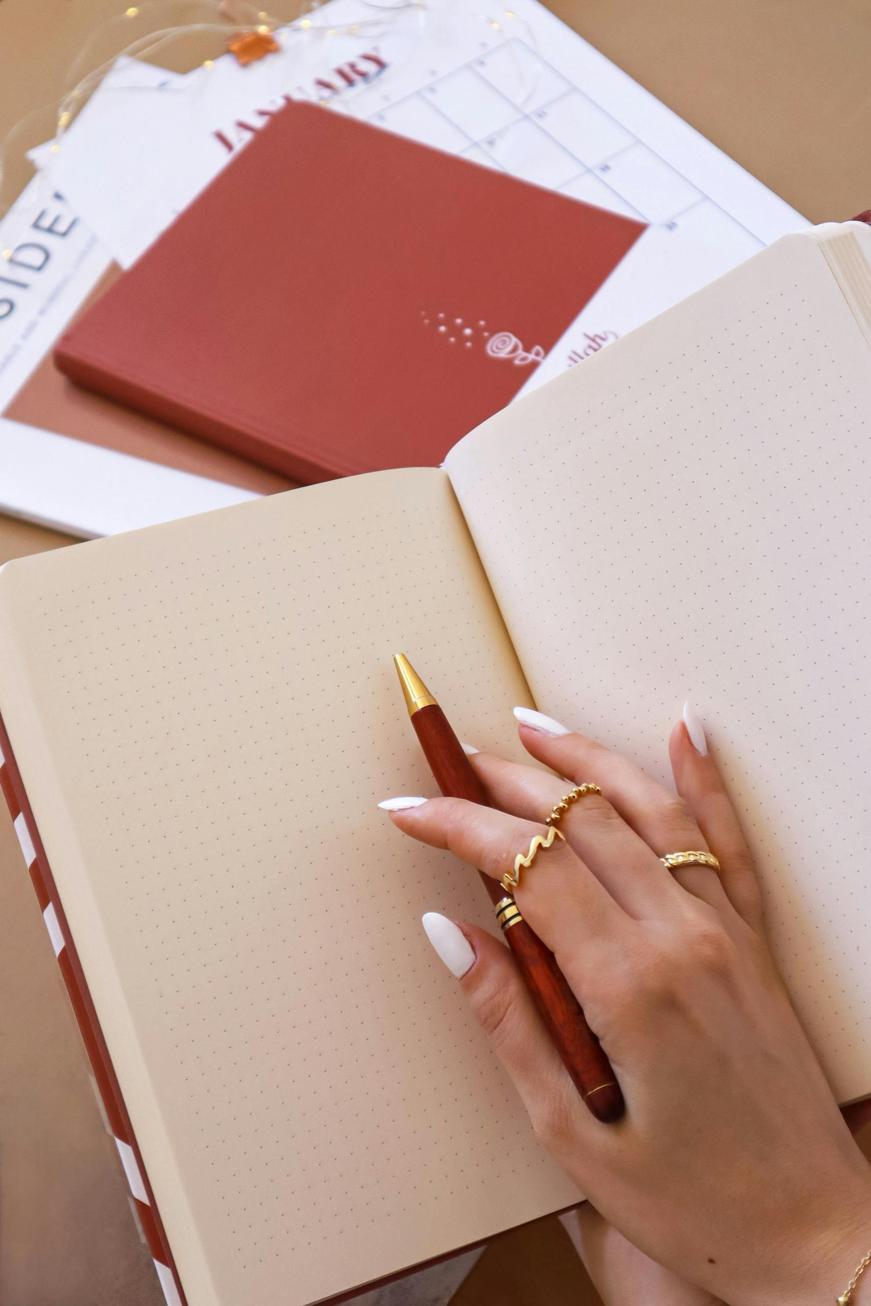 Close-up of a hand with manicured nails holding a pen and writing in an open notebook.